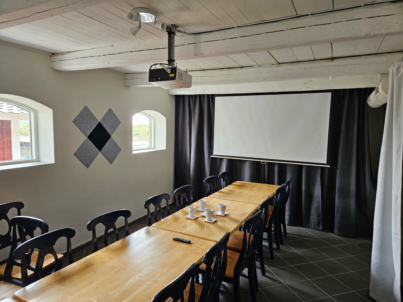 Konferensbord dukat med kaffekoppar framför projektorduken